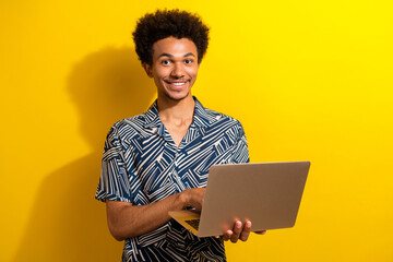Smiling young man with a laptop in a patterned shirt against a vibrant yellow background