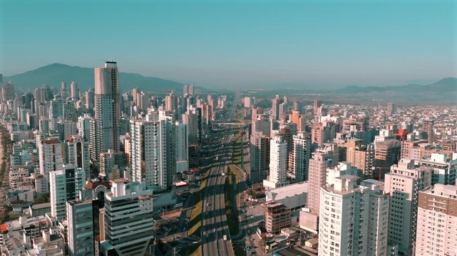 Aerial view of Avenida Nereu Ramos flanked by dense high-rises in Itapema, Santa Catarina, Brazil, with distant mountains, coastal skyline, and urban expansion clearly visible.