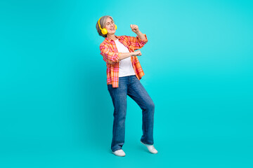 Elderly woman joyfully dancing with headphones on a vibrant turquoise background showcasing a fun...
