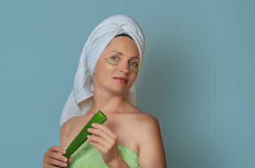 Woman with natural aloe vera patches for wellness and care. Towel on head, aloe leaf in hands.