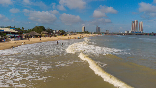 Aerial view of sun-kissed sands meet the rolling waves at a beach near clustered buildings, a vibrant blend of nature and architecture, Lagos, Lagos, Nigeria.