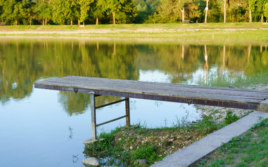 Wooden dock extends into calm lake surrounded by lush greenery during daytime