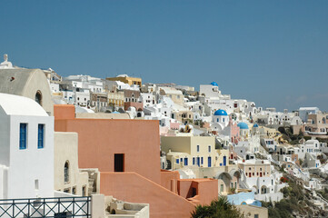 Fototapeta premium Wide view of Thira’s white buildings perched along the cliffs of Santorini, with a deep blue sea and clear sky in the background. A postcard-perfect Greek island scene.