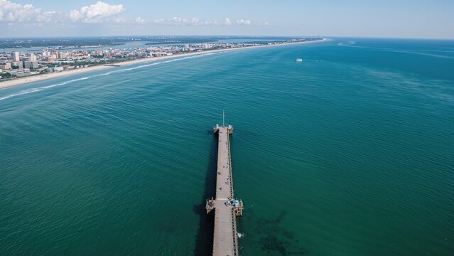 A remarkably elongated jetty projects into the ocean, captured from a lofty drone vantage point above a coastal island.