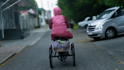 Obraz premium Person in pink raincoat riding a tricycle down a quiet street on a rainy day