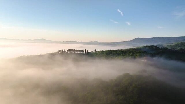 Aerial view of a landscapes by Bagno Vignoni, shrouded in ethereal fog, with trees and buildings emerging from the mist in soft sunrise hues, Tuscany, Italy.