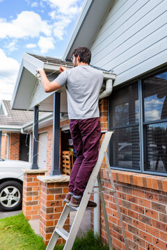 Man up ladder in front of house stringing fairy lights for Christmas decorations