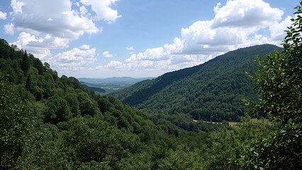 Obraz premium Panoramic view of lush green hills with dense forests under a blue sky with clouds in the background during daytime in a mountainous region