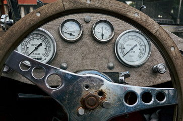 The steering wheel of a vintage car has a few gauges on it