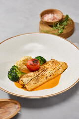 Cod fillet with grilled vegetables and sauce, bright lighting, minimal overhead composition