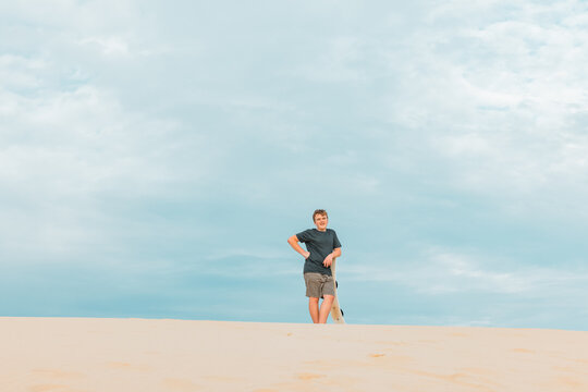 Boy leaning on sand board on top of dune at Birubi Beach, Port Stephens