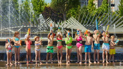 Water launch. Group of children playing in park fountain with water pistols on sunny day. Concept of splash toy campaign, water safety education for schools, fun zone branding for kids parks