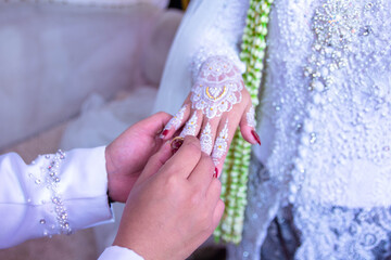 The hand of an Asian man  is attaching a wedding ring to the hand of an Asian woman at a wedding...