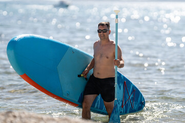 Man entering sea with stand up paddle board on sunny day