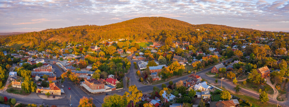 Aerial view of golden hour lighting over a tree covered mountain behind a small rural town