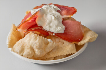 Traditional Tuscan fried dough bites called coccoli topped with prosciutto crudo and creamy burrata mozzarella, served on a white plate with natural light and white background.