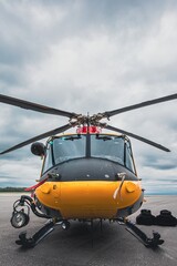 Fototapeta premium SAR helicopter on an airport apron under cloudy skies, vertical image with rotor blades extended and search and rescue equipment on the ground. Dramatic sky with clouds fills the background.