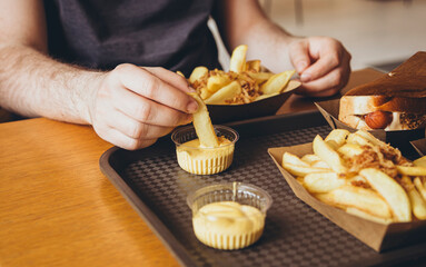 A man eats crispy potatoes with cheese sauce in a pub or fast food cafe.