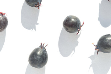 Fresh serviceberries on white background casting shadows in minimalist composition.