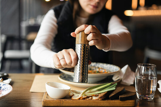 A woman in a restaurant adds pepper or salt to her dish.