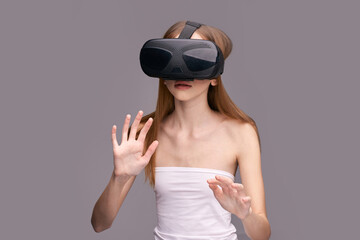 Young caucasian female immersed in virtual reality experience with vr headset on gray background.