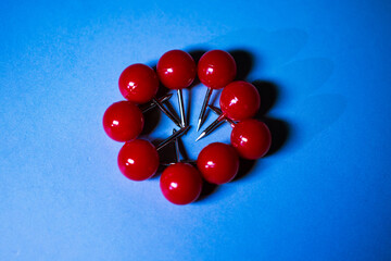 Bright red push pins arranged in a circular pattern on a bold blue background. The vibrant contrast...