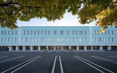 Modern light blue administrative building with large windows under autumn foliage and spacious parking lot