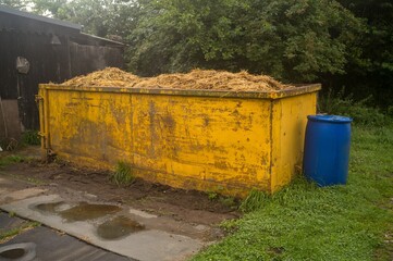 Yellow container overflowing with dry straw near farm building