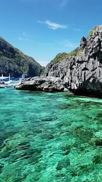 Traditional boats docked by the cliffs in turquoise waters of El Nido, Palawan. El Nido boats near rocks and crystal clear reef in Palawan, Philippines from above, vertical screen