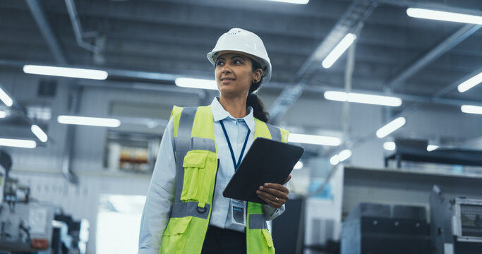 Portrait of a Latin Female Worker in a White Hard Hat Walking Through a Modern, Well-lit Factory, Inspecting Advanced Industrial Machinery, Checking Equipment, Overviewing Production