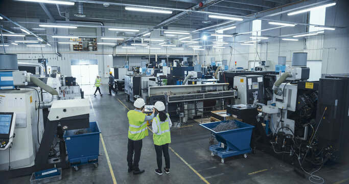 Male Factory Technologist and Female Industrial Engineer Using Augmented Reality Software at Work. Worker Pointing Interactive Camera on a Tablet Computer at a Heavy Duty CNC Machinery