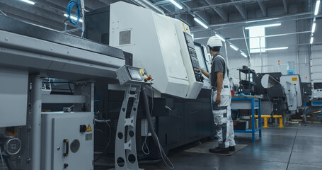 Asian Male Engineer in a White Hard Hat Operating a CNC Milling Machine in a Modern Factory. Young Technician Inserting Parameters into the Computer, Automating Production Line