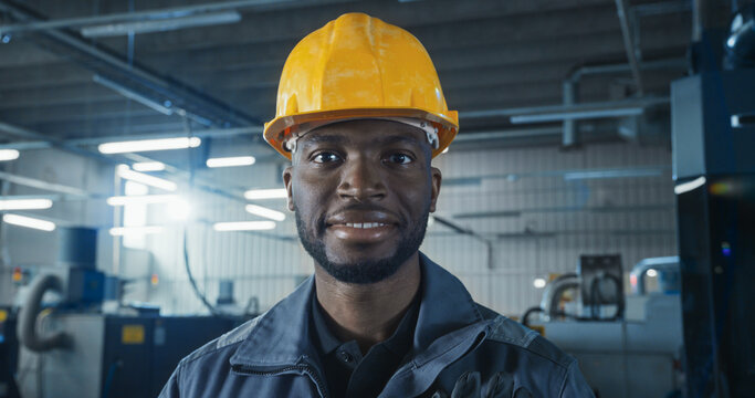 Cinematic Portrait of an African American Man at Work in a Factory. Handsome Black Male Posing for Camera, Looking at Viewer, Smiling. Worker Operating Heavy Duty Machinery, Using Technical Skills