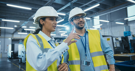Manufacturing Process Manager and Equipment Supervisor Having a Meeting on Factory Floor, Discussing Production Technology, Strategic Business Partnerships, Metal Component Delivery Techniques