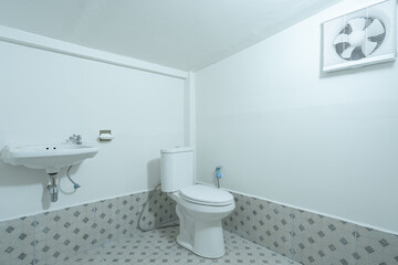 The toilet has a sink there are grey patterned tiled floor and ventilation fan. The room is in white tones.