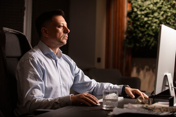 Focused man in a light shirt holds smartphone while working at a stylish evening office. Modern...