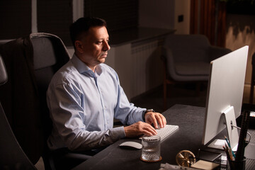 Focused man in a light shirt holds smartphone while working at a stylish evening office. Modern...