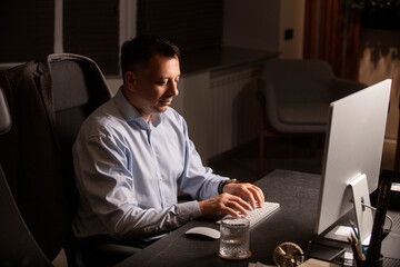 Focused man in a light shirt holds smartphone while working at a stylish evening office. Modern...