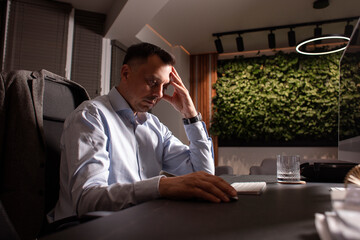 Focused man in a light shirt holds smartphone while working at a stylish evening office. Modern...