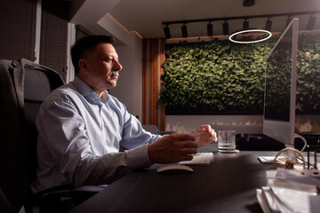 Focused man in a light shirt holds smartphone while working at a stylish evening office. Modern...