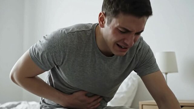 Man face contorted clutches stomach in pain Bedroom setting