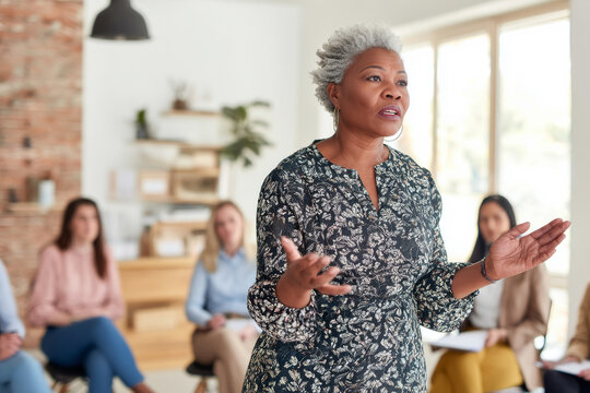 A mature Black woman teaches a conflict resolution workshop, using role-playing techniques and active listening exercises to strengthen emotional intelligence among department leads