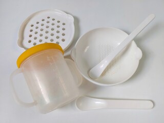 White Set of children's bowls, mug, grater and spoons on the white background. Baby tableware. Nutrition and first level Baby's feeding concept