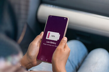 Running out of battery while on the go. A muslim woman in car holding a smartphone with low battery symbol on screen.