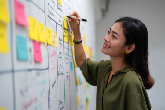 A young adult Asian businesswoman updates client personas in a customer journey map, incorporating market research and survey data to refine targeting strategies and improve satisfaction
