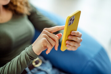 Woman using smartphone with yellow case at home, representing casual lifestyle and indoor comfort