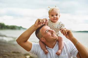 father and baby child girl at the sunset on the waterscape view from back