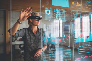 A middle-aged Caucasian woman interacts with digital graphs via AR glasses, navigating smart data in a cutting-edge tech office environment.