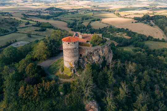 Aerial view of Ch&Atilde;&cent;teau de Buss&Atilde;&copy;ol, a medieval castle rising from a verdant hilltop against a backdrop of rolling fields and distant hills, Buss&Atilde;&copy;ol, Auvergne-Rh&Atilde;&acute;ne-Alpes, France.
