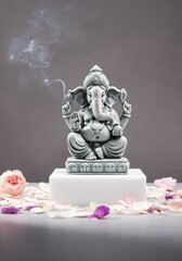 A gray statue of Lord Ganesha sits on a white pedestal. Surrounding it are pink and white flower petals. Smoke rises from an incense stick nearby.
